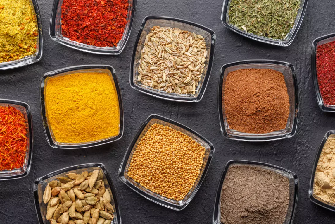 An overhead view of glass bowls filled with various dried herbs and spices—perfect for building a basic kitchen spices list.