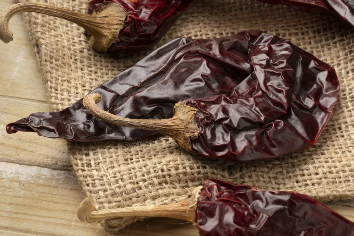 Close-up of dried red chile pods on a rustic burlap cloth, showing their deep red color and wrinkled texture, great for making red chile sauces, enchilada sauces, tamales, birria, posole, and more.