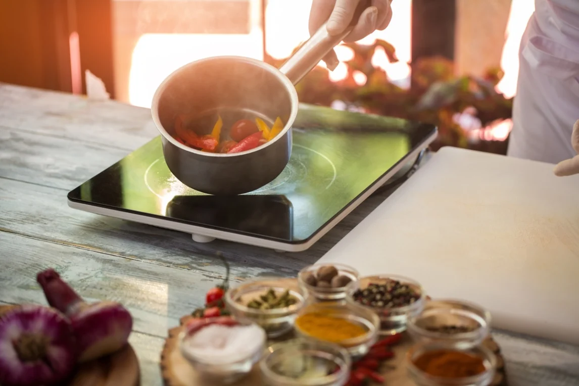 Chef holding a saucepan over a cooktop with bell peppers steaming inside, surrounded by jars of colorful spices and herbs on a rustic table—highlighting salt-free cooking with low sodium seasoning blends.