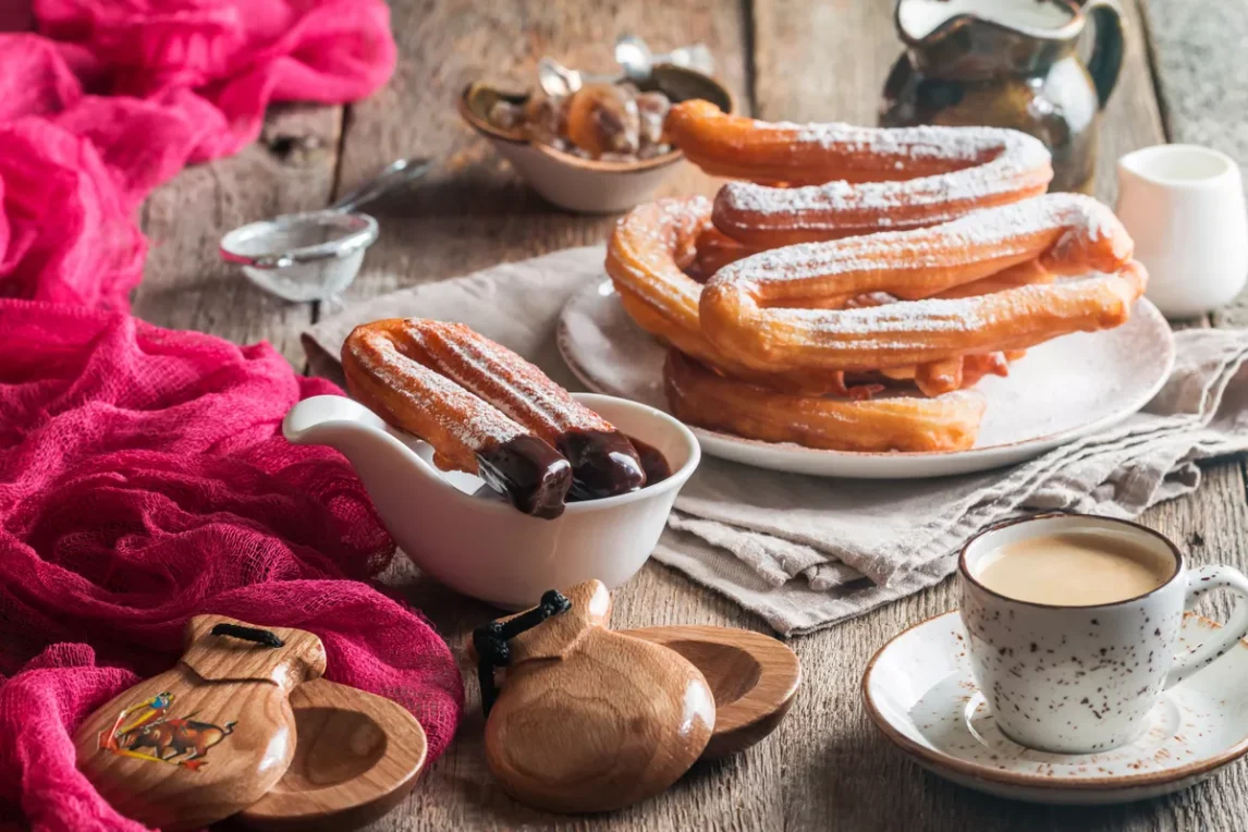 A plate of golden churros dusted with cinnamon sugar, dipped in chocolate sauce, and served with coffee.